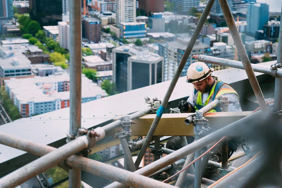A worker on scaffolding high above a city skyline.