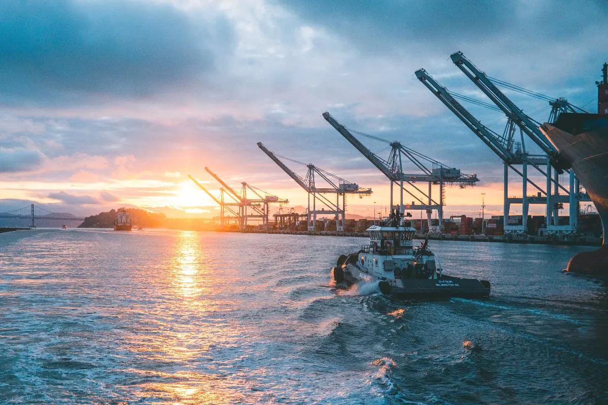 Container terminal cranes at sunset with a tug in the foreground.