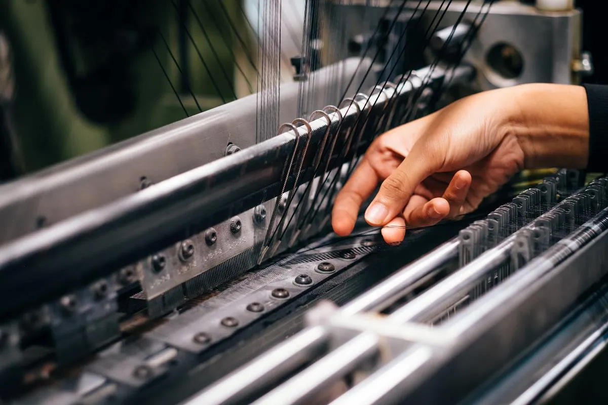 A hand adjusting threads on a textile loom.