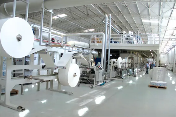 Une ligne de production de produits d'hygiène, avec de grands rouleaux de matière blanche alimentant les machines.