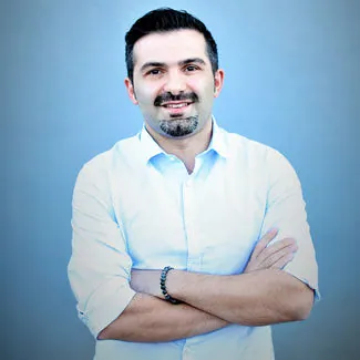 Portrait d'Osman Taşkan en chemise claire, les bras croisés.