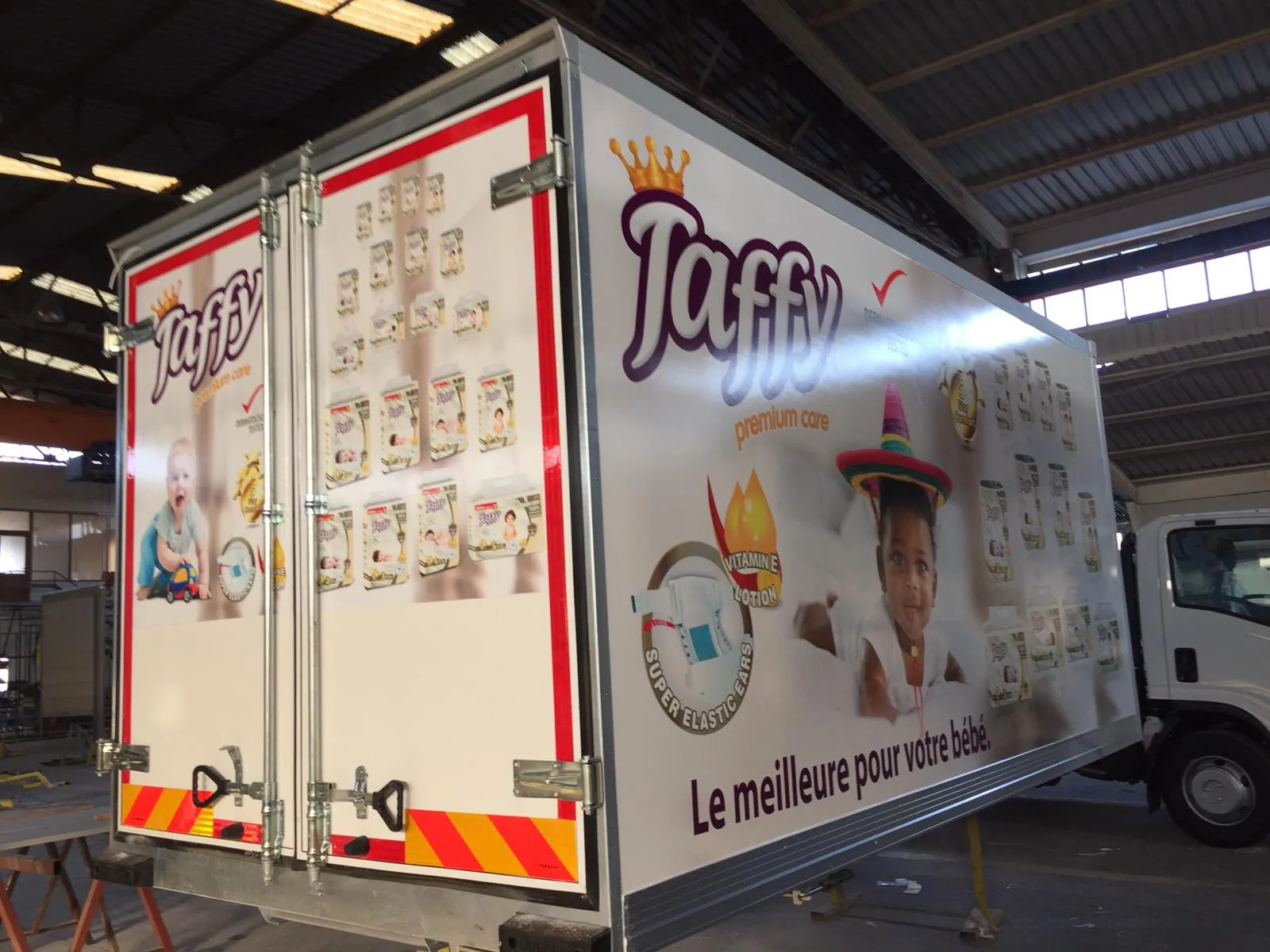 Camion de livraison aux couleurs de Taffy, avec des paquets de couches imprimés sur le flanc et la mention « Le meilleure pour votre bébé ».